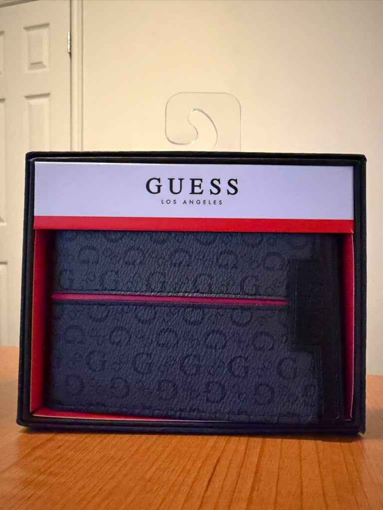 Billetera Guess color negro con monograma G, diseño plegable, múltiples compartimentos para tarjetas y billetes, detalle de línea roja frontal, presentación original en caja, ideal para uso diario o regalo.