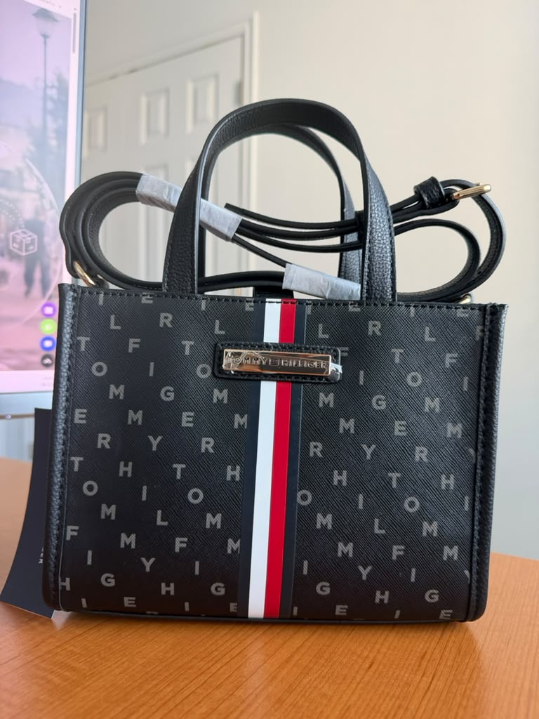 Bolso compacto con diseño elegante en color negro, estampado del logo y detalle frontal en los colores icónicos de la marca. Incluye correa ajustable para usar al hombro o cruzado. Ideal para el día a día.